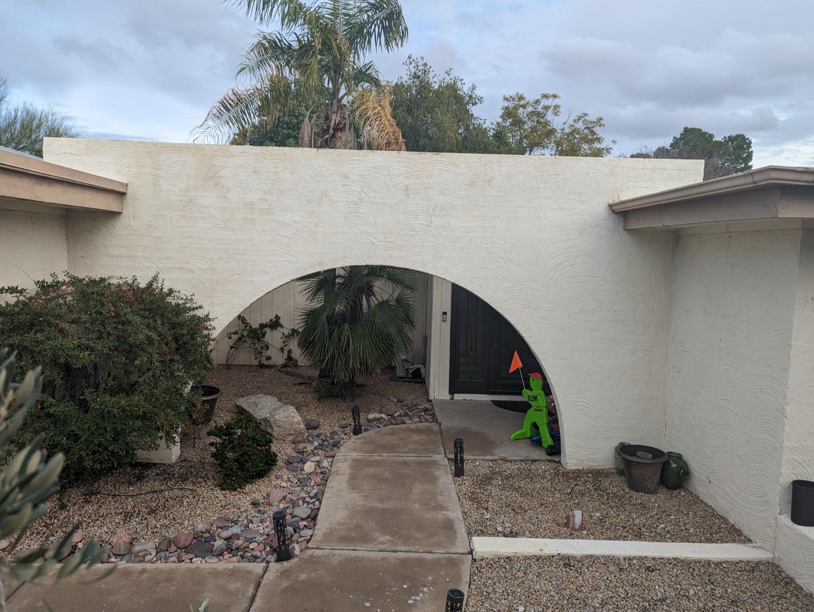 Mission project entry courtyard before — weathered stucco arch with cluttered walkway